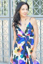 Woman wearing a colorful floral dress standing in front of a geometric-patterned wall.