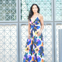 Woman wearing a colorful floral silk dress standing in front of a geometric-patterned wall.