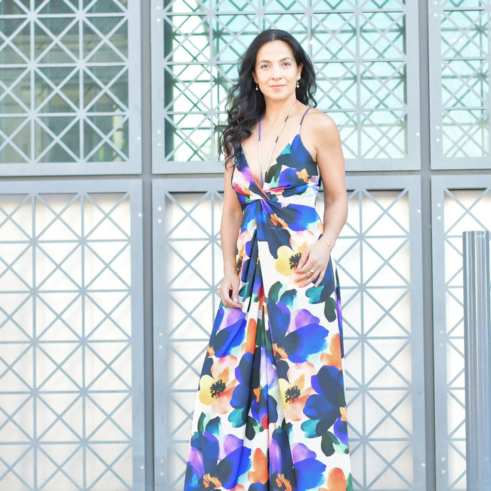 Woman wearing a colorful floral silk dress standing in front of a geometric-patterned wall.