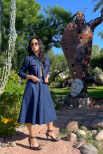 Woman in a blue dress standing in front of a large sculpture in a garden setting.