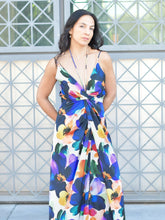 Woman wearing a colorful floral dress standing against a geometric-patterned wall.