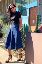 Woman in a black top and blue skirt standing next to a sculpture outdoors.