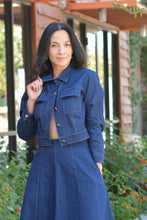Woman in a blue coat standing against a wall with greenery in the background