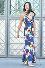 Woman wearing a colorful floral dress standing in front of a geometric-patterned wall.